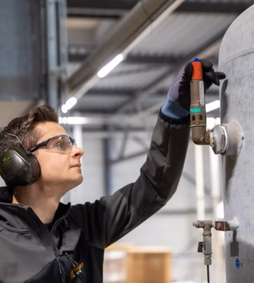 Un employé effectue une inspection sur un réservoir industriel dans un environnement de production.