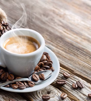 Een kop koffie staat tussen koffiebonen op een houten tafel.