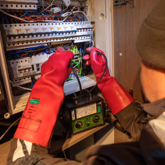 Elektrische Überprüfung eines Verteilerkastens mit Messgeräten und isolierten Handschuhen.