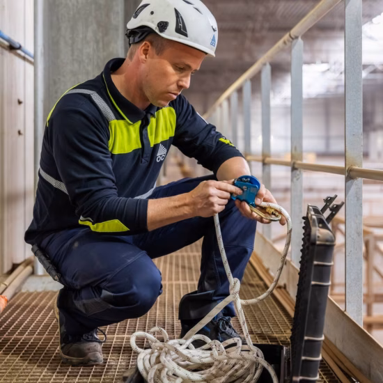 Medewerker inspecteert en ordent valbeveiligingslijn en veiligheidsmateriaal op een verhoogd werkplatform.