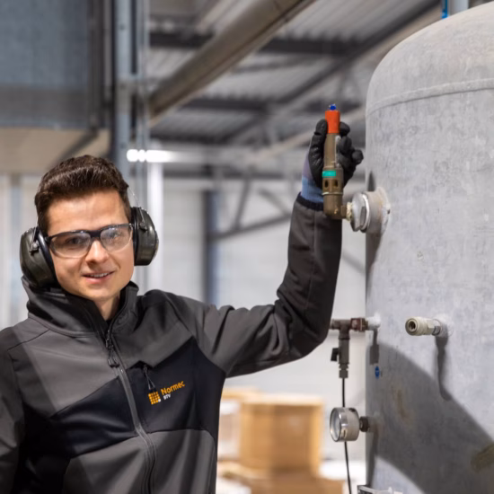 Medewerker met gehoorbescherming en veiligheidsbril voert een inspectie uit bij een industriële installatie.