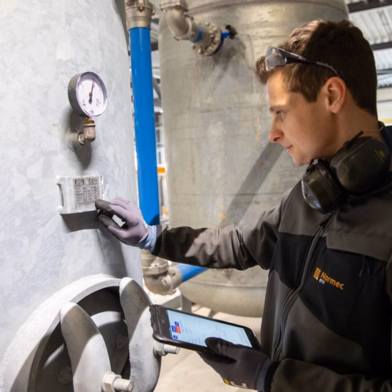 Technisch inspecteur controleert een industriële installatie met manometer en meetapparatuur in een technische ruimte.