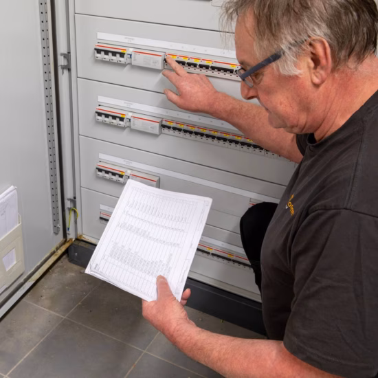 Inspecteur controleert een elektrische verdeelkast aan de hand van een inspectierapport.