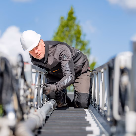 Technicus voert inspectie uit aan een industriële installatie op hoogte en controleert leidingwerk.