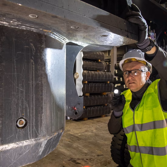 Inspecteur in veiligheidsvest controleert een industriële installatie en voert een meting uit bij een machineonderdeel.