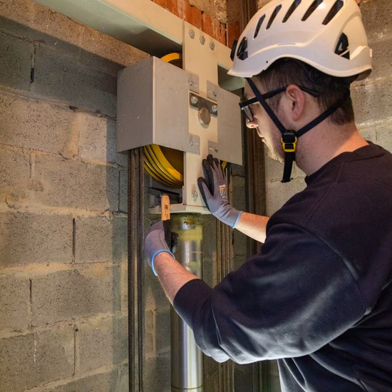 Technisch medewerker voert inspectie uit aan een besturingskast bij een liftschacht.