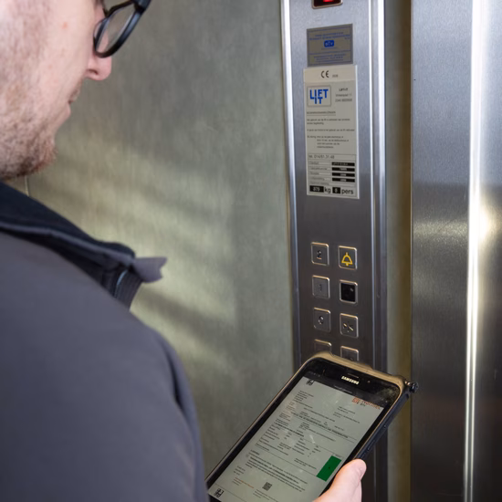 Technicus controleert een liftinstallatie met een tablet bij het bedieningspaneel van een lift.
