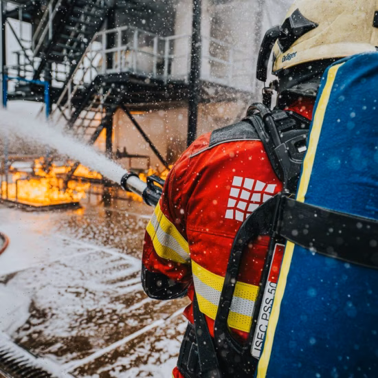 A firefighter fights an industrial fire with a fire hose during a practical drill or emergency response at an industrial park.