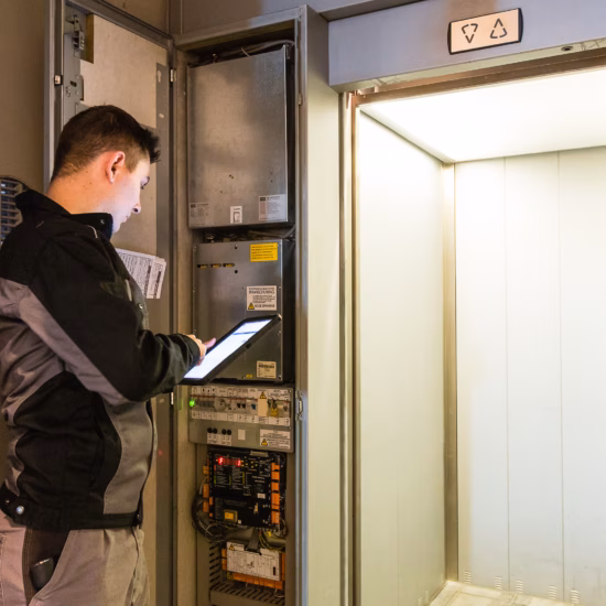 Un employé effectue une inspection technique au niveau du boîtier de commande d'un ascenseur.