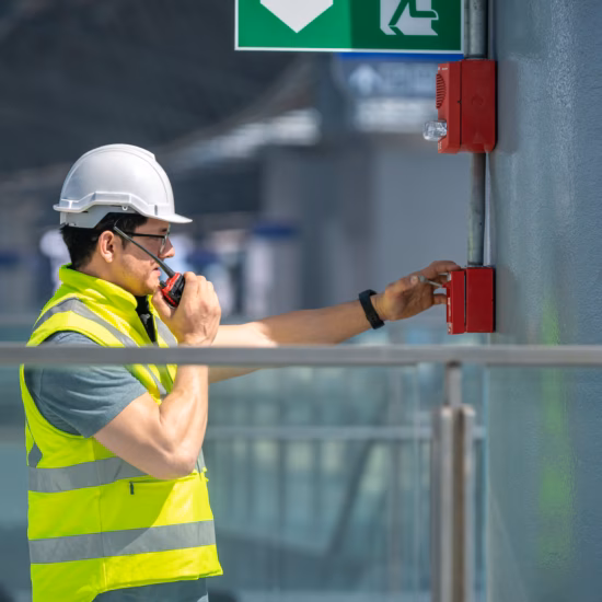 Normec technician wearing a white safety helmet and a high-visibility vest while inspecting fire safety systems in a commercial building.