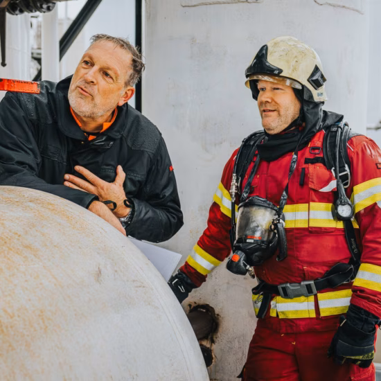 Firefighter in full protective gear discussing fire safety measures with a colleague in a building.