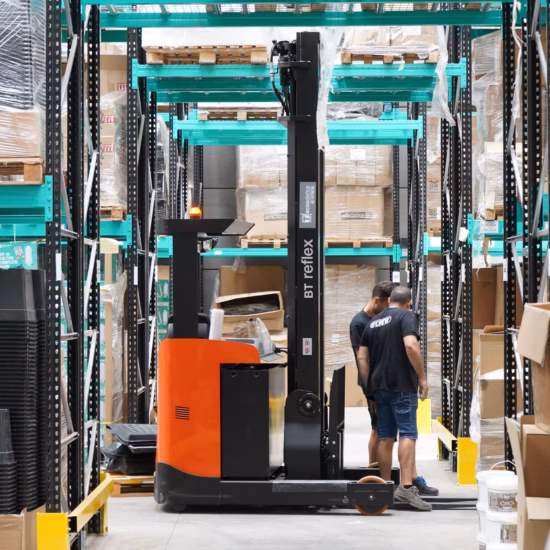 Een medewerker werkt met een smallegangtruck in een magazijn met hoge stellingen en opgeslagen goederen.
