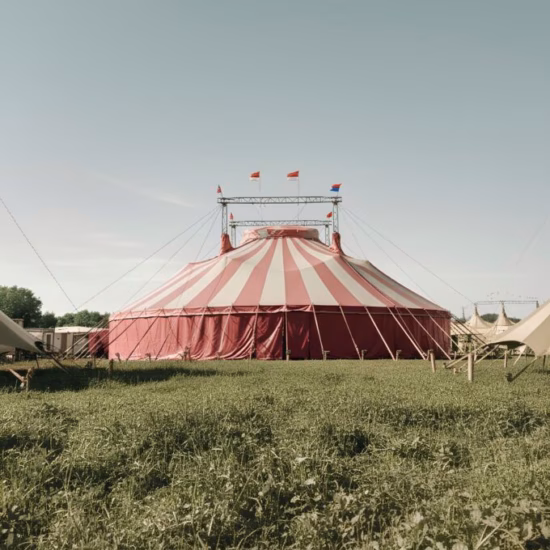 Een rood-wit gestreepte circustent staat op een open grasveld onder een heldere lucht.