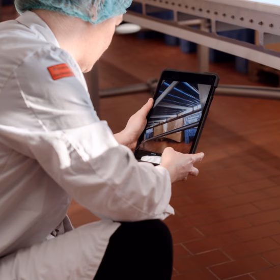 Een medewerker controleert de conditie van een vloer met behulp van een tablet in een productieomgeving.