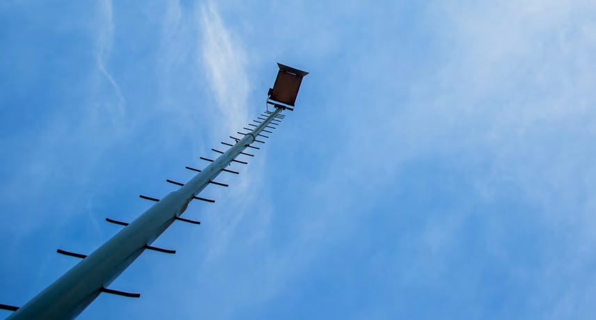 Ein hoher Mast mit Plattform hebt sich vom strahlend blauen Himmel ab.