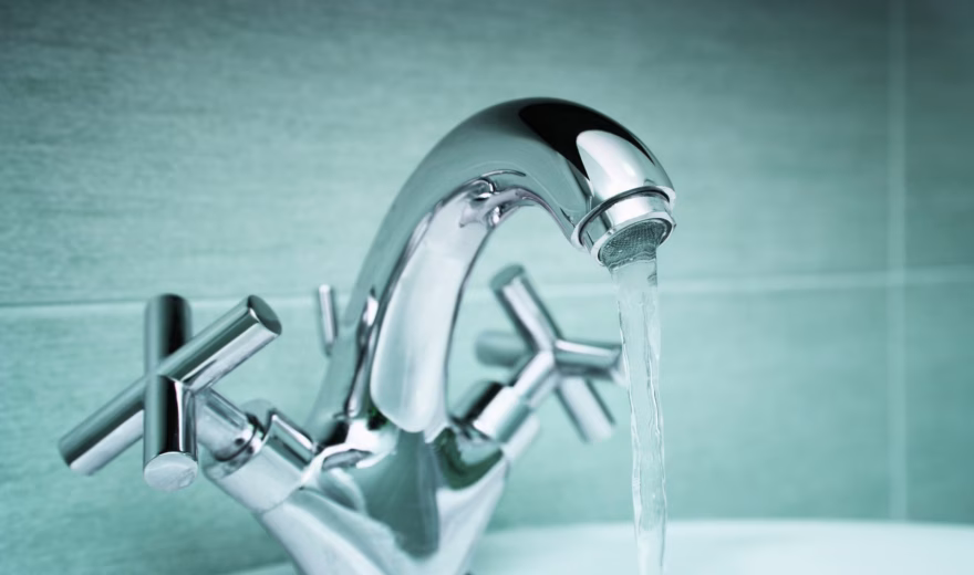 Kraan met stromend water boven een wastafel in een badkamer.
