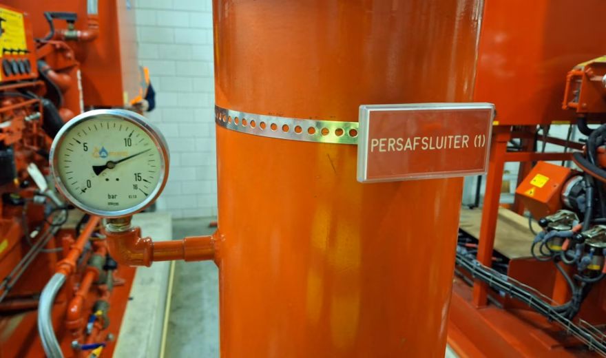 Persafsluiter op een oranje leidinginstallatie met manometer in een technische ruimte.
