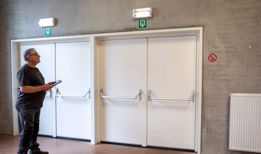 Inspecteur controleert nooddeuren en vluchtwegen in een gebouw met behulp van een tablet.