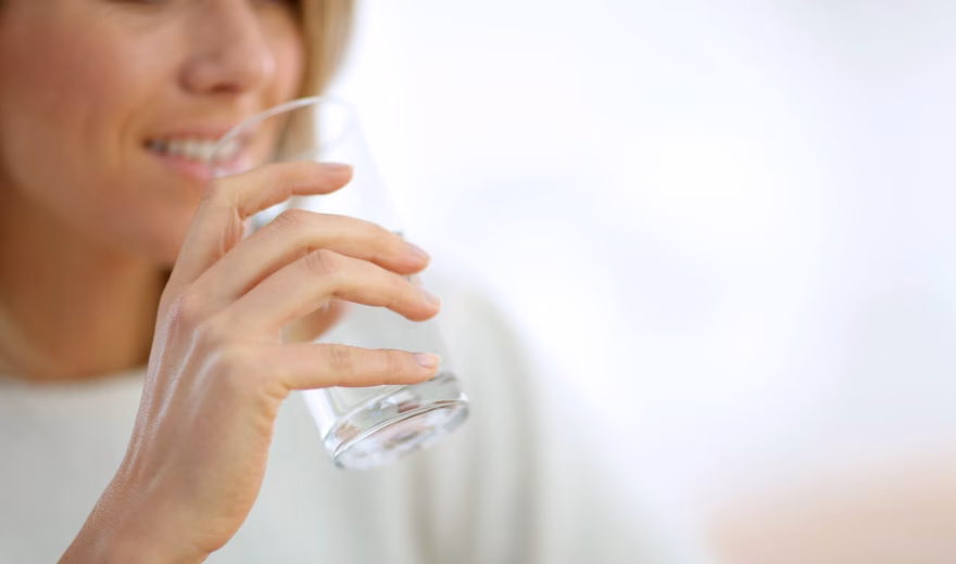 Persoon drinkt een glas water in een lichte binnenomgeving.