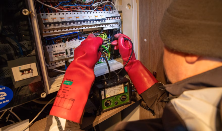 Ein Elektrotechniker führt mit Schutzhandschuhen eine Isolationswiderstandsmessung in einem Sicherungskasten durch.