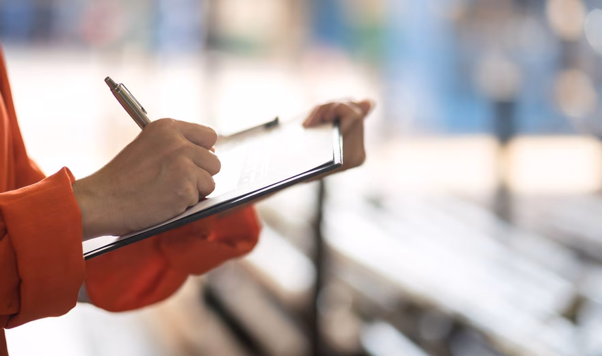 Une personne note les données d'inspection sur un bloc-notes lors d'un contrôle dans un environnement industriel.