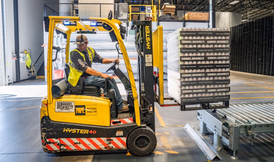 Een heftruckchauffeur transporteert goederen in een magazijn met industriële opslagstellingen.