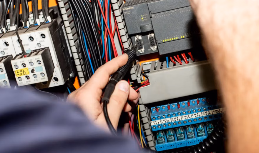 Un technicien effectue des mesures dans une armoire électrique ouverte contenant des câbles et des composants.