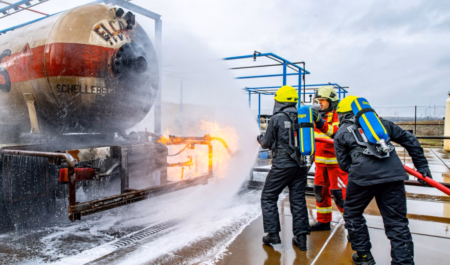 Einsatzkräfte bekämpfen bei einem Vorfall auf einem Außengelände einen Brand mit Schaum und Wasser.