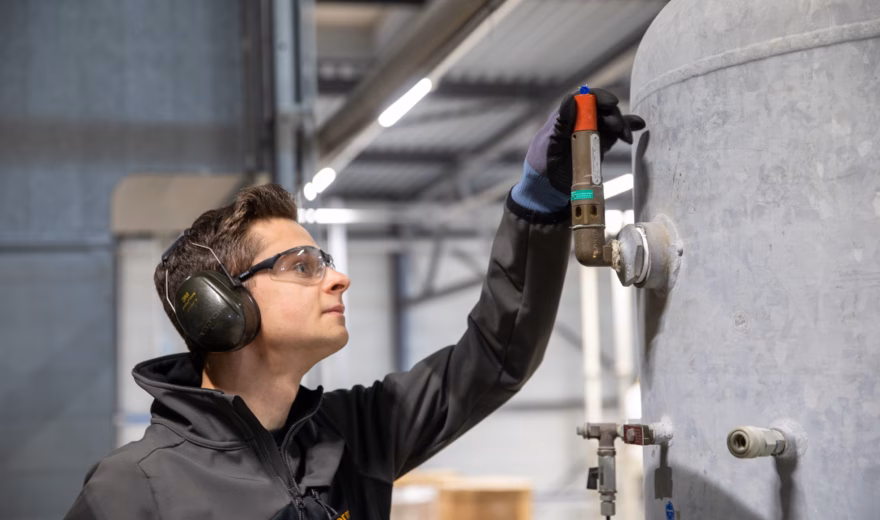 Een medewerker voert een controle uit aan een industriële tank in een productieomgeving.