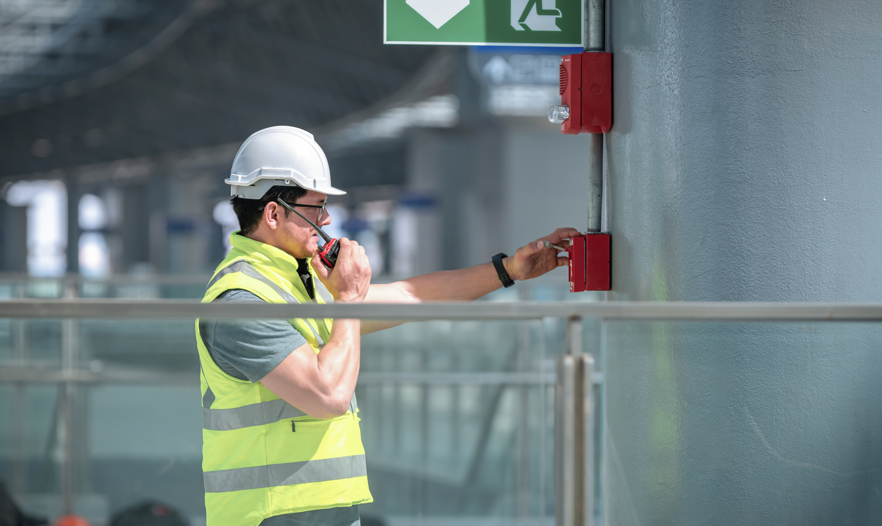 Medewerker test een handbrandmelder als onderdeel van een brandmeldinstallatie in een gebouw.