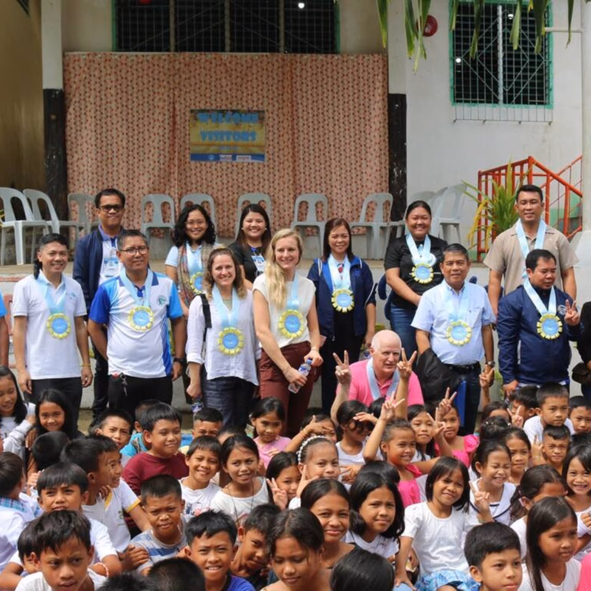 A large group of children and adults poses together in front of a building during a social or educational event.
