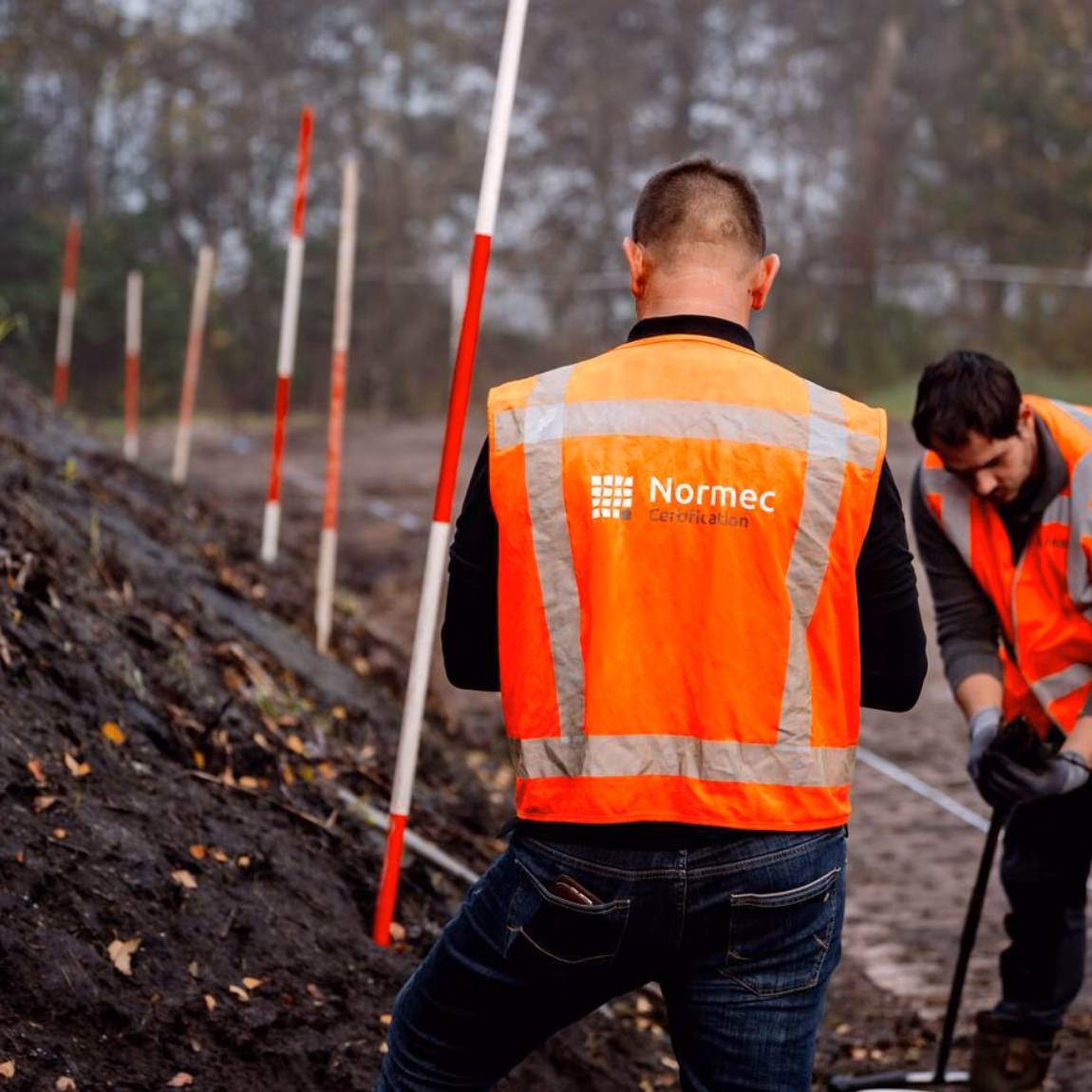 Employees wearing safety vests are conducting fieldwork at a soil investigation site using measuring equipment.