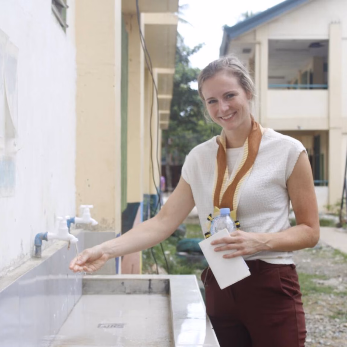 A person is conducting a hygiene or water inspection at an outdoor sink, holding a notepad.