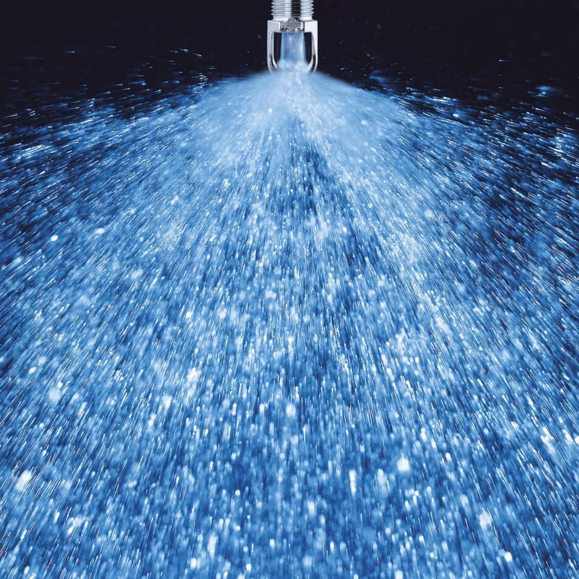 Wassernebel aus einer Sprühdüse während eines industriellen Reinigungs- oder Produktionsprozesses.