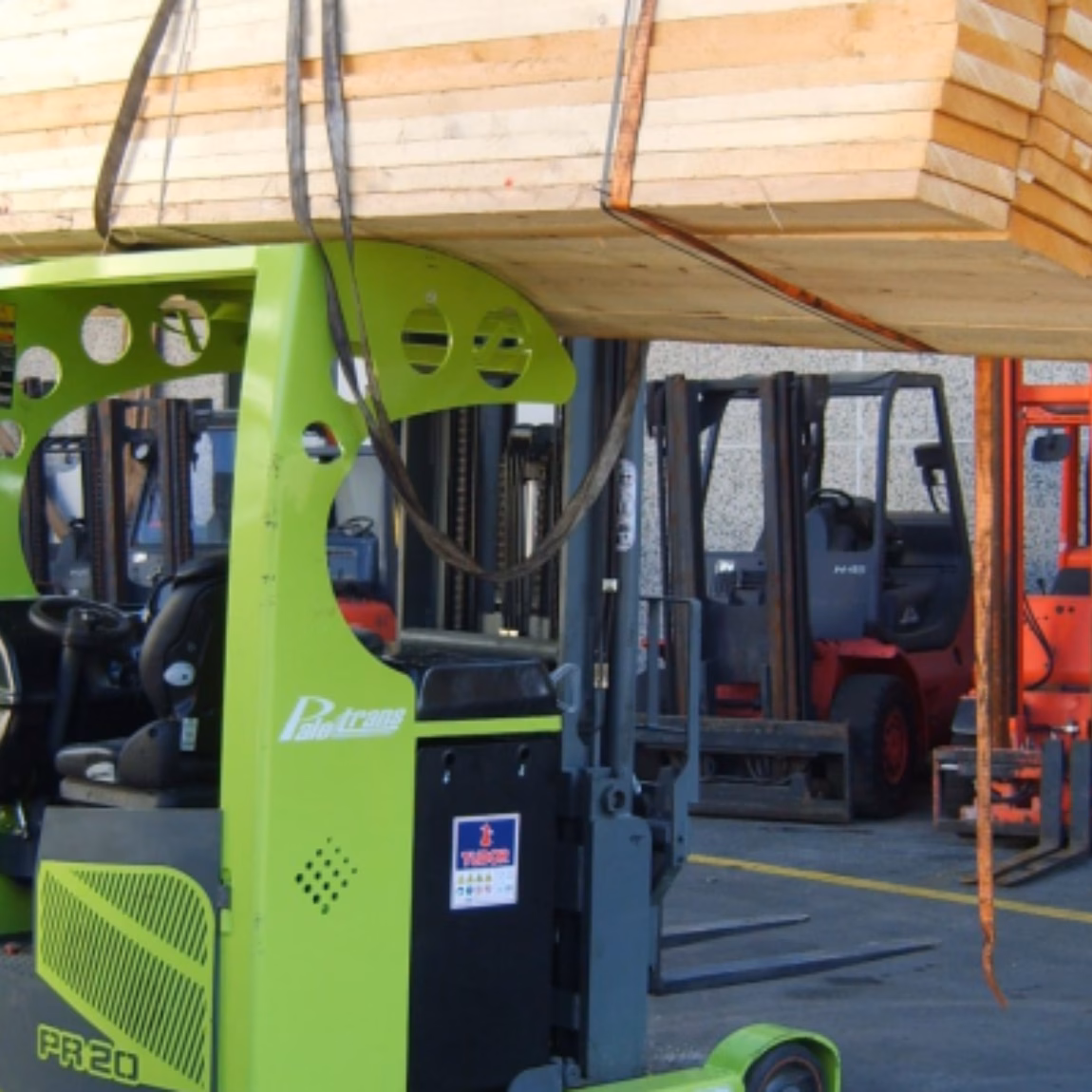 Ein Industriegabelstapler hebt und transportiert auf einem Lagerhof einen großen Stapel Holzbretter, die mit Hebegurten gesichert sind. Dabei stehen der sichere Materialumschlag, der Transport schwerer Lasten, Lagerabläufe, logistische Effizienz und qualitätskontrollierte industrielle Prozesse im Vordergrund.
