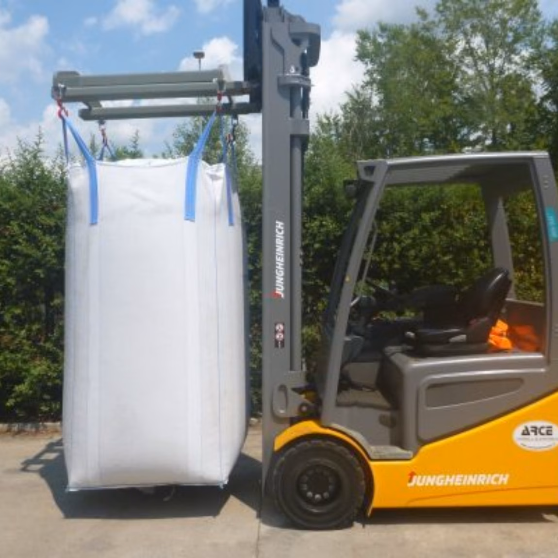 Ein Gabelstapler transportiert einen großen industriellen Schüttgut-Sack mithilfe eines speziellen Hubaufsatzes in einem Logistikbereich im Freien, wobei der Schwerpunkt auf sicherem Materialumschlag, Schüttguttransport, Lagereffizienz, Qualitätssicherung und industriellem Lieferkettenmanagement liegt