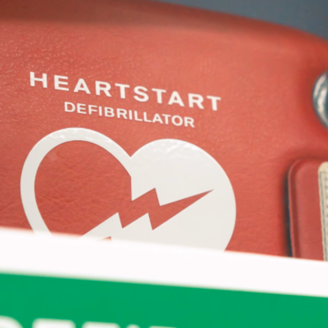Nahaufnahme eines automatisierten externen Defibrillators (AED) mit deutlichen Notfallkennzeichnungen, die die Sicherheit am Arbeitsplatz, die Notfallvorsorge, die Erste-Hilfe-Bereitschaft und lebensrettende medizinische Geräte in professionellen Umgebungen hervorheben.
