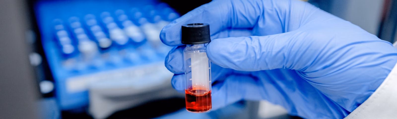 Laboratoriumhandschoen houdt een reageerbuisje met rode vloeistof vast voor laboratoriumapparatuur voor monstertesten.