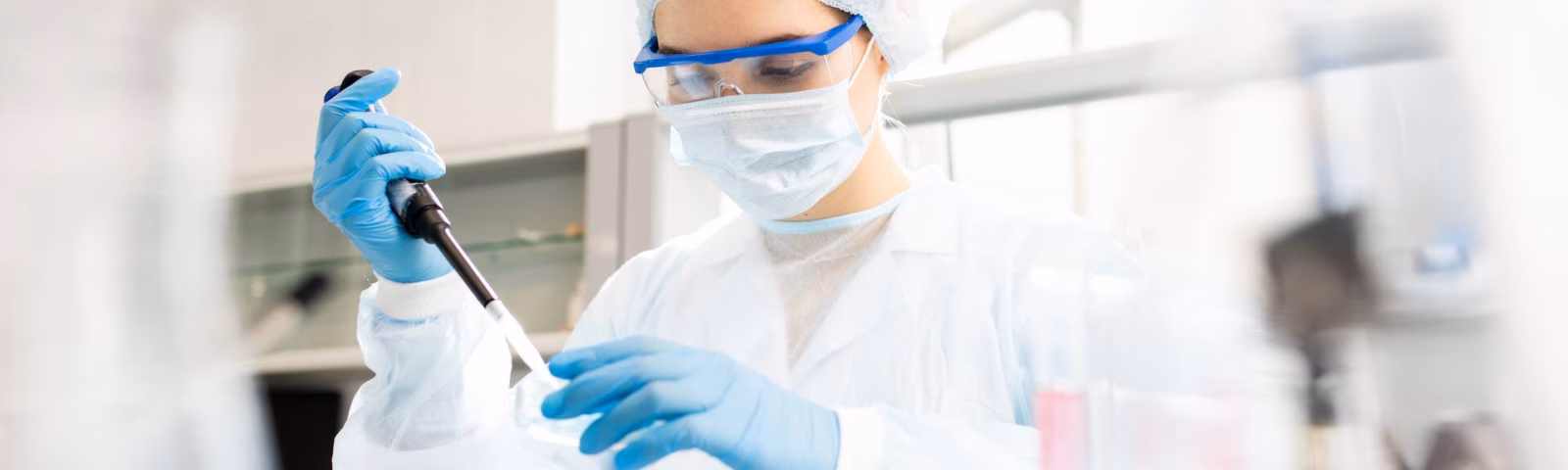 A laboratory technician wearing sterile protective clothing performs a pipetting procedure during a laboratory analysis.