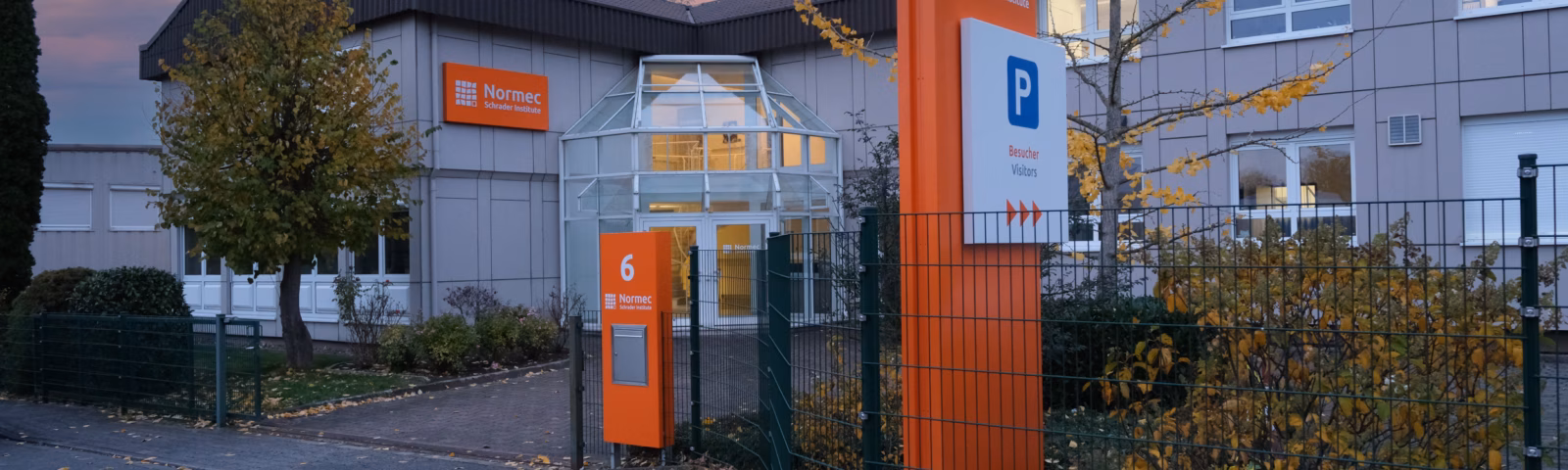 Exterior view of a modern research and testing center featuring brand-specific signage, gate-secured access, and a parking lot reserved for visitors, reflecting a professional environment dedicated to scientific services and quality assurance.