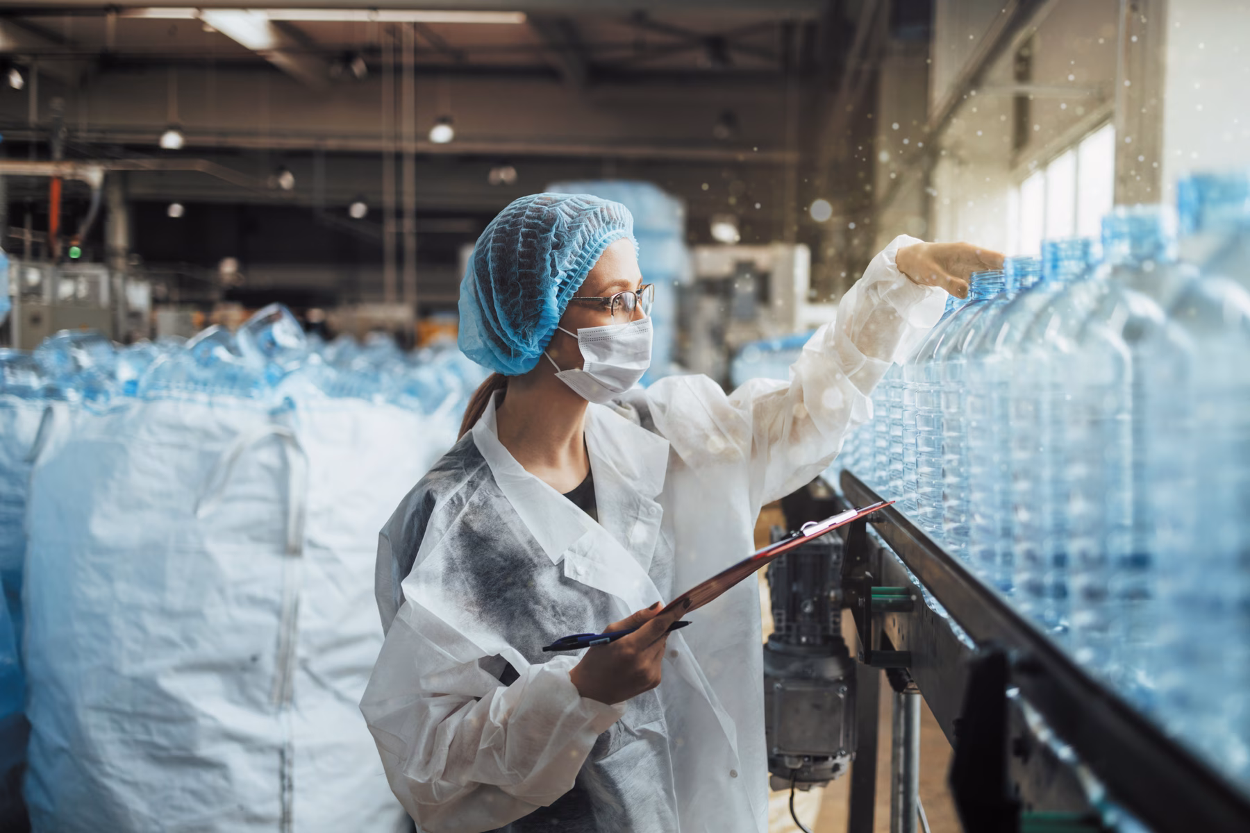 Medewerker controleert grote waterflessen aan een productielijn binnen een productie- of kwaliteitscontroleomgeving.