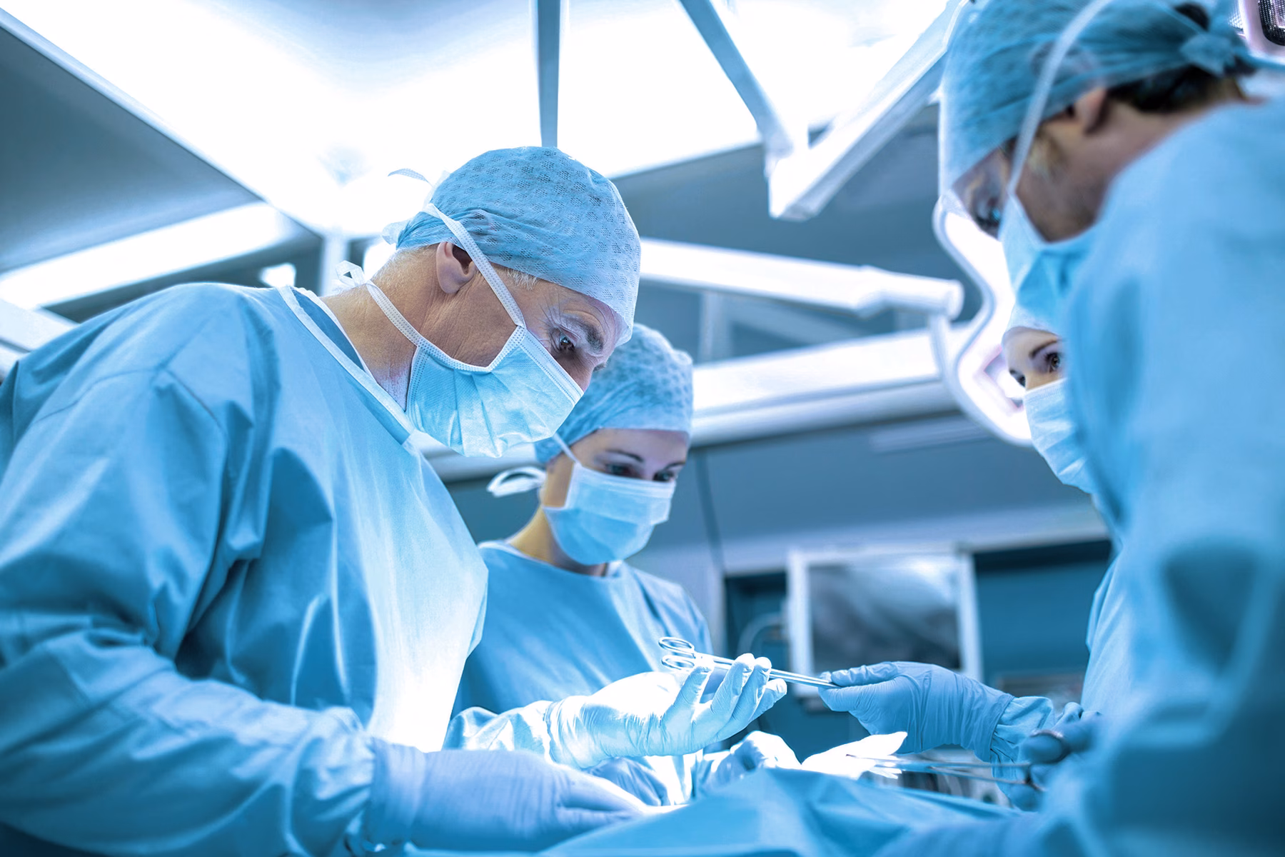 Operatieteam voert een medische ingreep uit in een operatiekamer met beschermende kleding en chirurgische apparatuur.