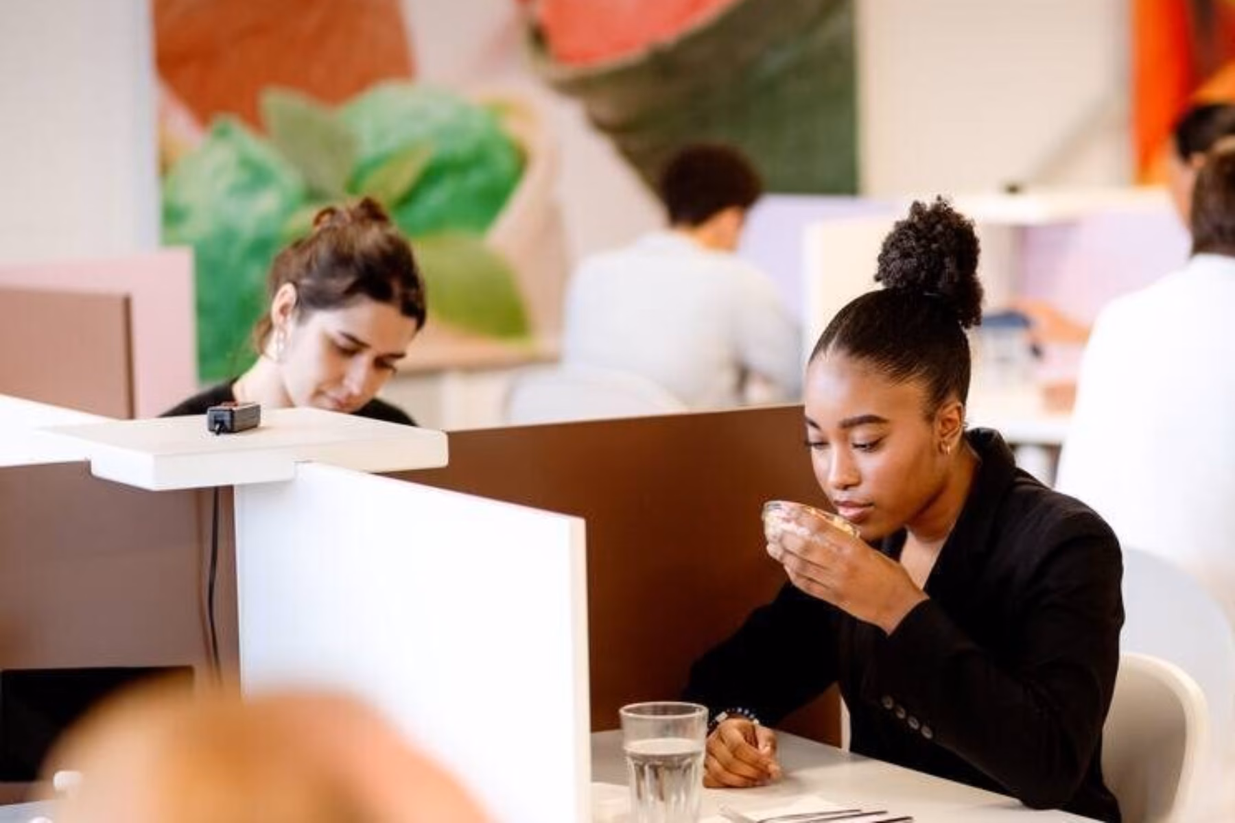 Two women are testing food in cubicles, with one woman smelling the food she is researching.