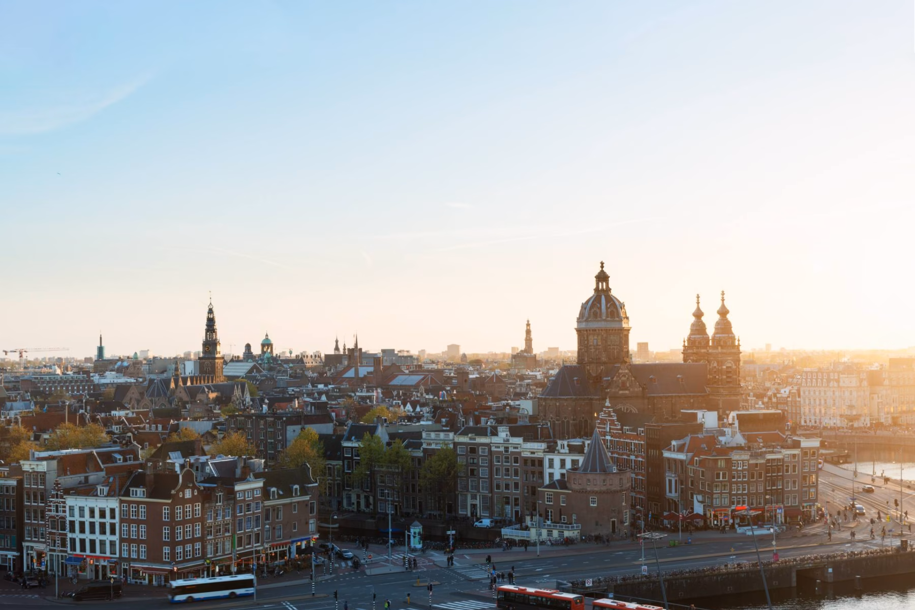 Elevated view of a city with sunlight, many buses on the streets, pedestrians walking, and beautiful buildings.