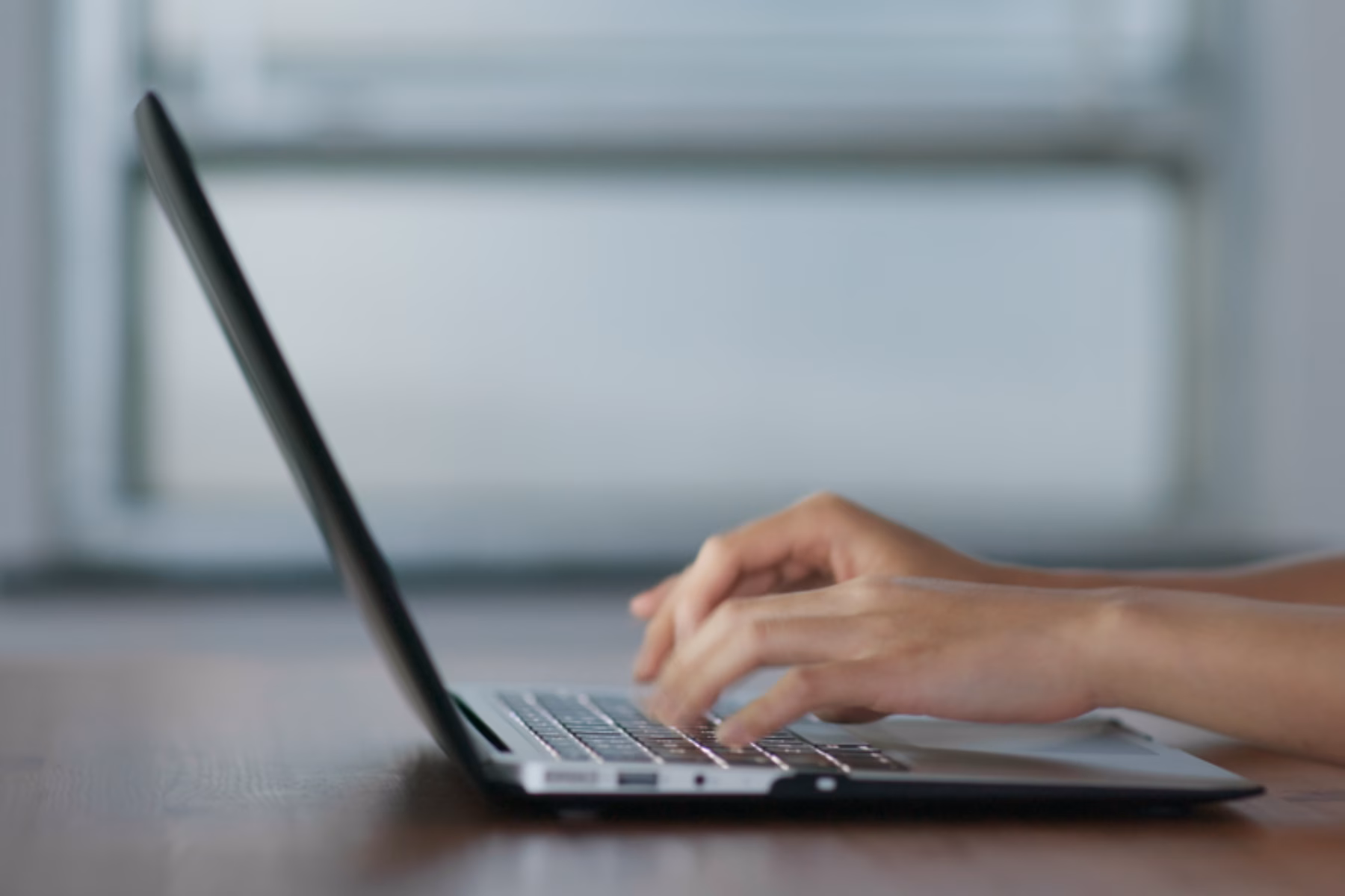 Close-up of hands typing on a laptop keyboard at a desk.