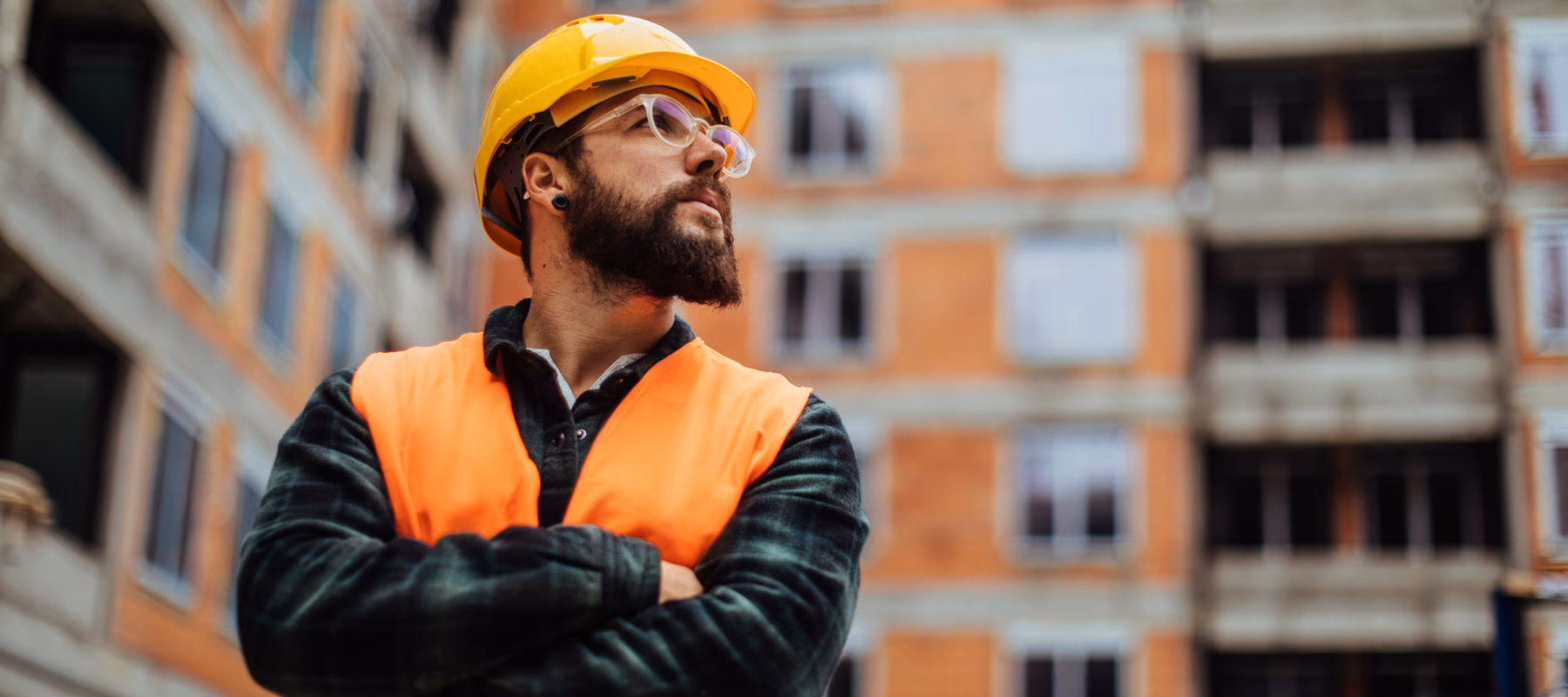 A man wearing a reflective vest and safety helmet is looking up and inspecting buildings.