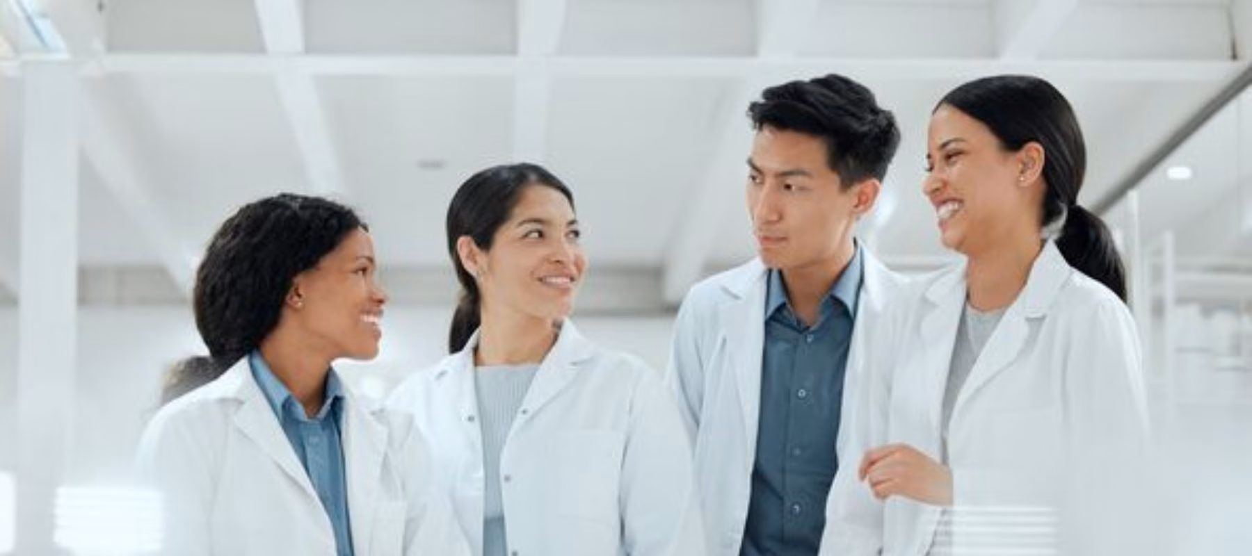 Four scientists in white lab coats smiling at each other.