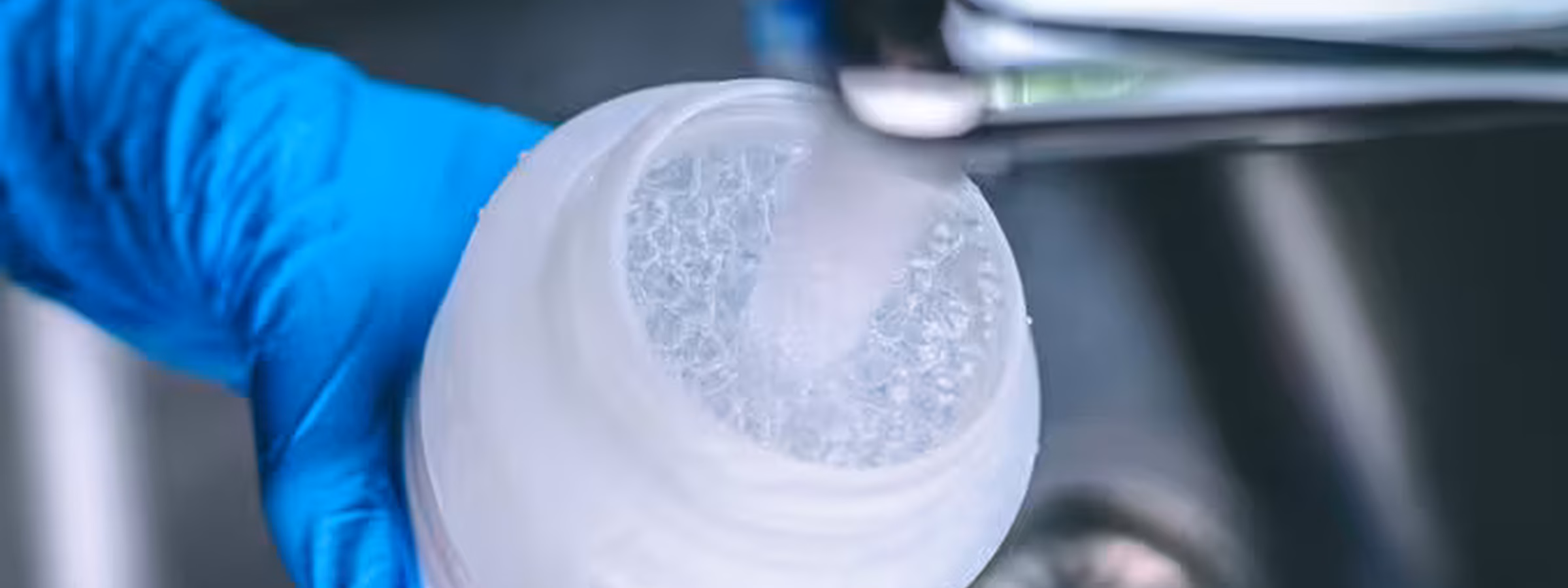 A gloved hand fills a sample jar with water from a faucet for laboratory testing or water analysis.