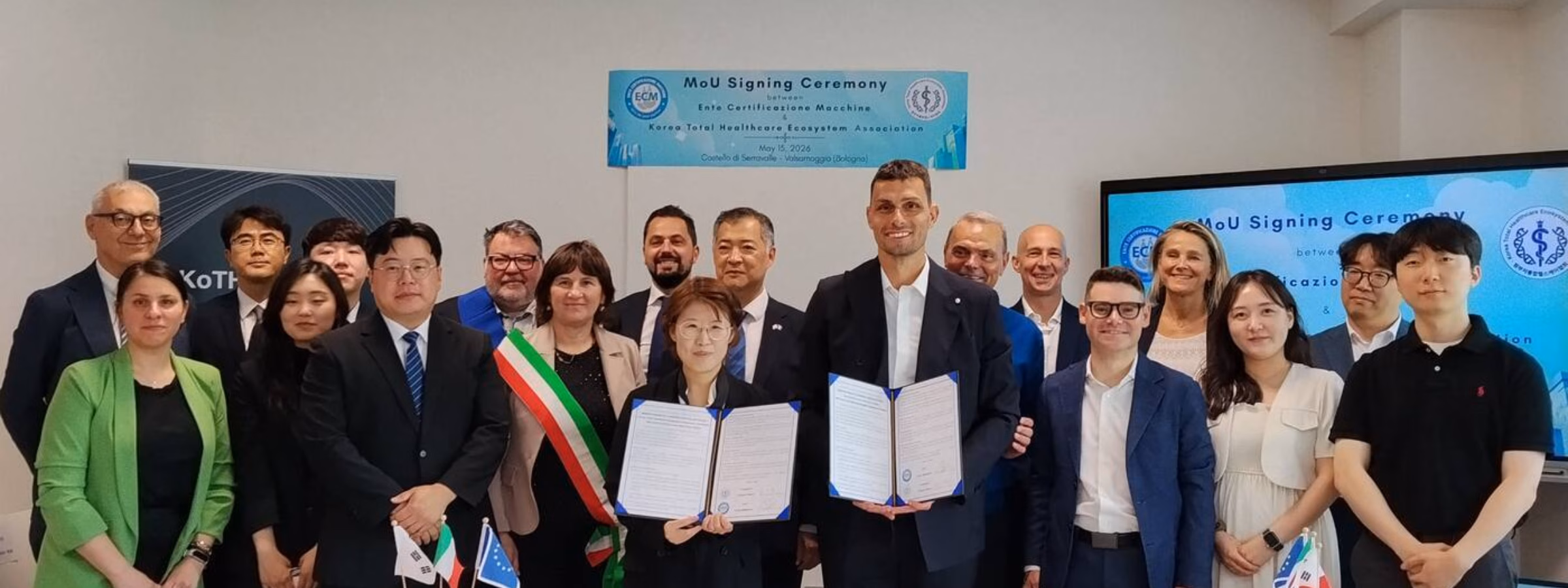 A group of participants poses with the signed documents during a formal gathering in a conference room.