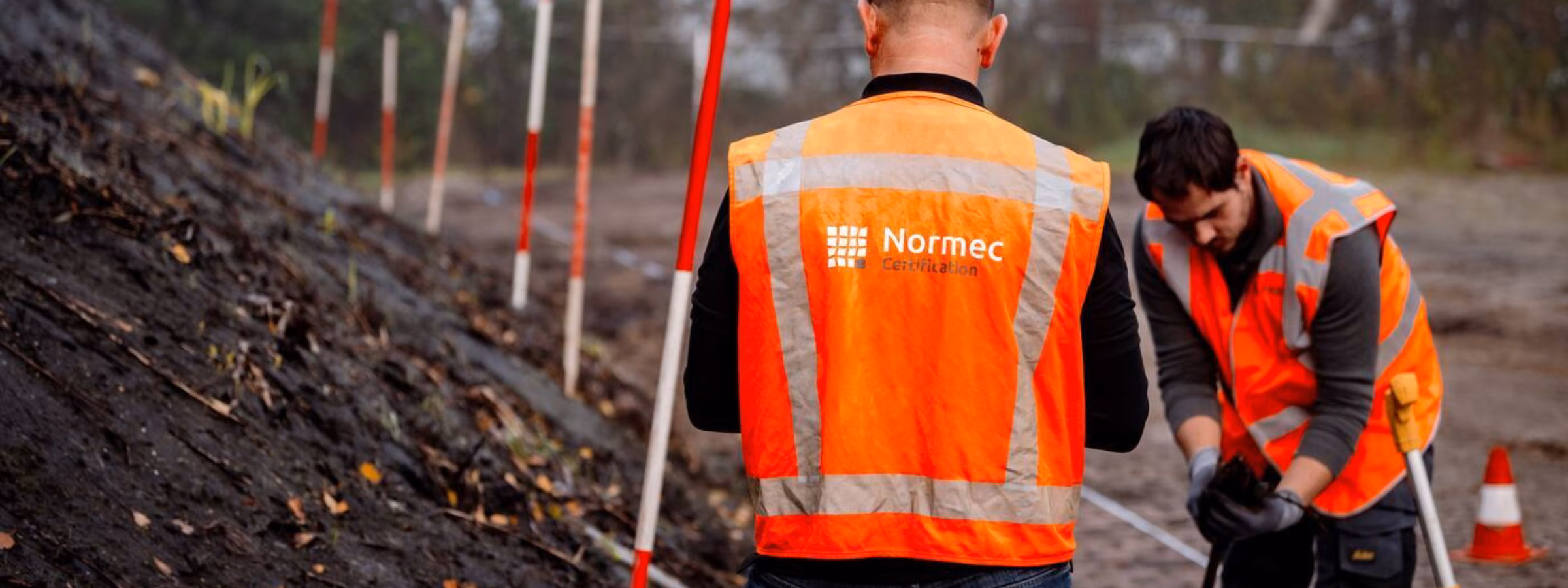 Employees wearing safety vests are conducting fieldwork at a soil investigation site using measuring equipment.